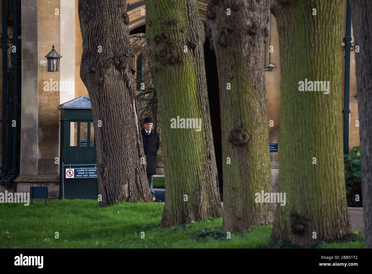A bowler hat wearing security guard stands at an entrance to Trinity College, Cambridge, UK. Stock Photo