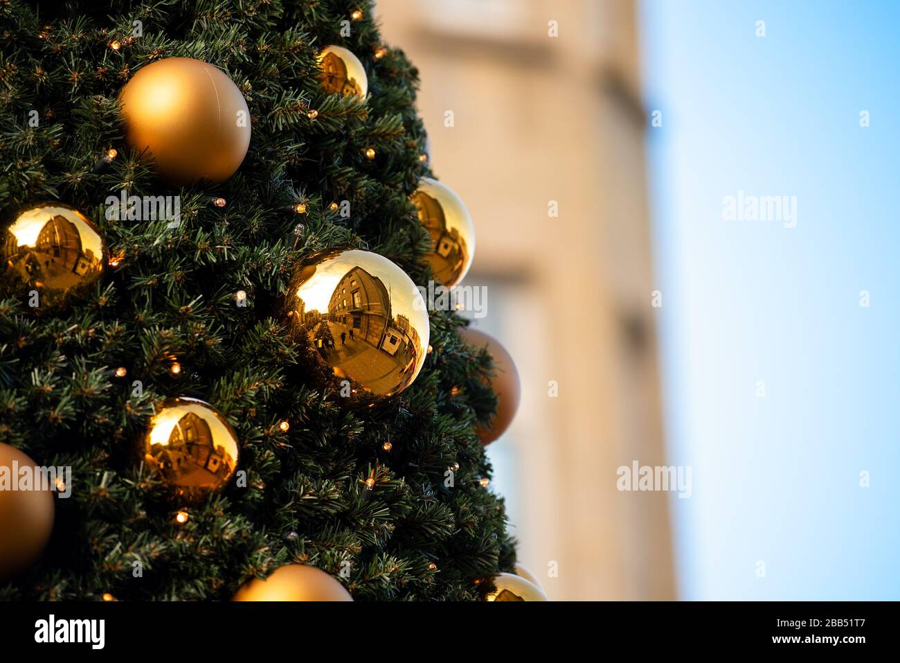 Golden decorative baubles hanging in a Christmas tree reflect the surround outdoor buildings. Stock Photo