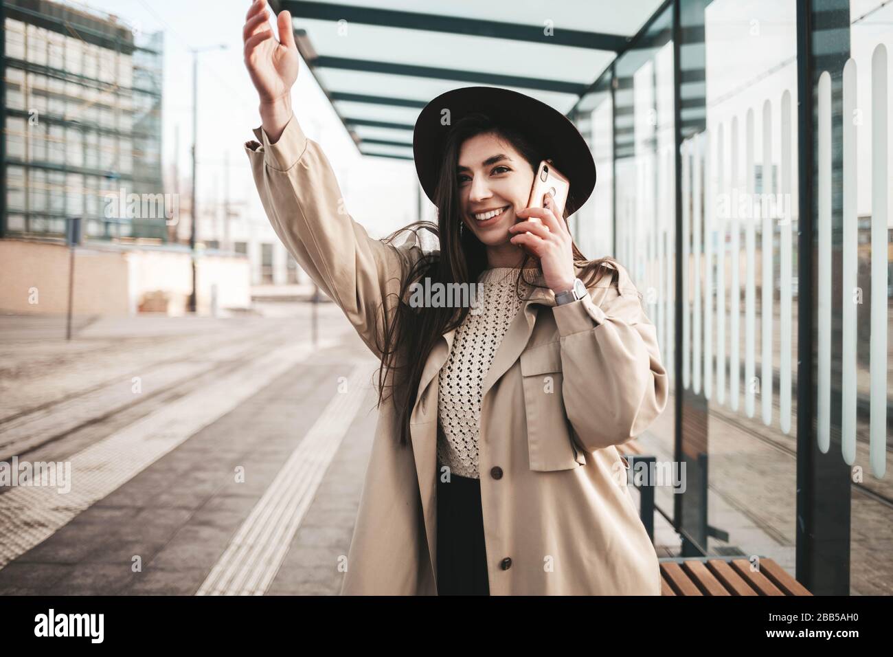 Girl talking on the phone and waving while standing at the bus stop Stock Photo