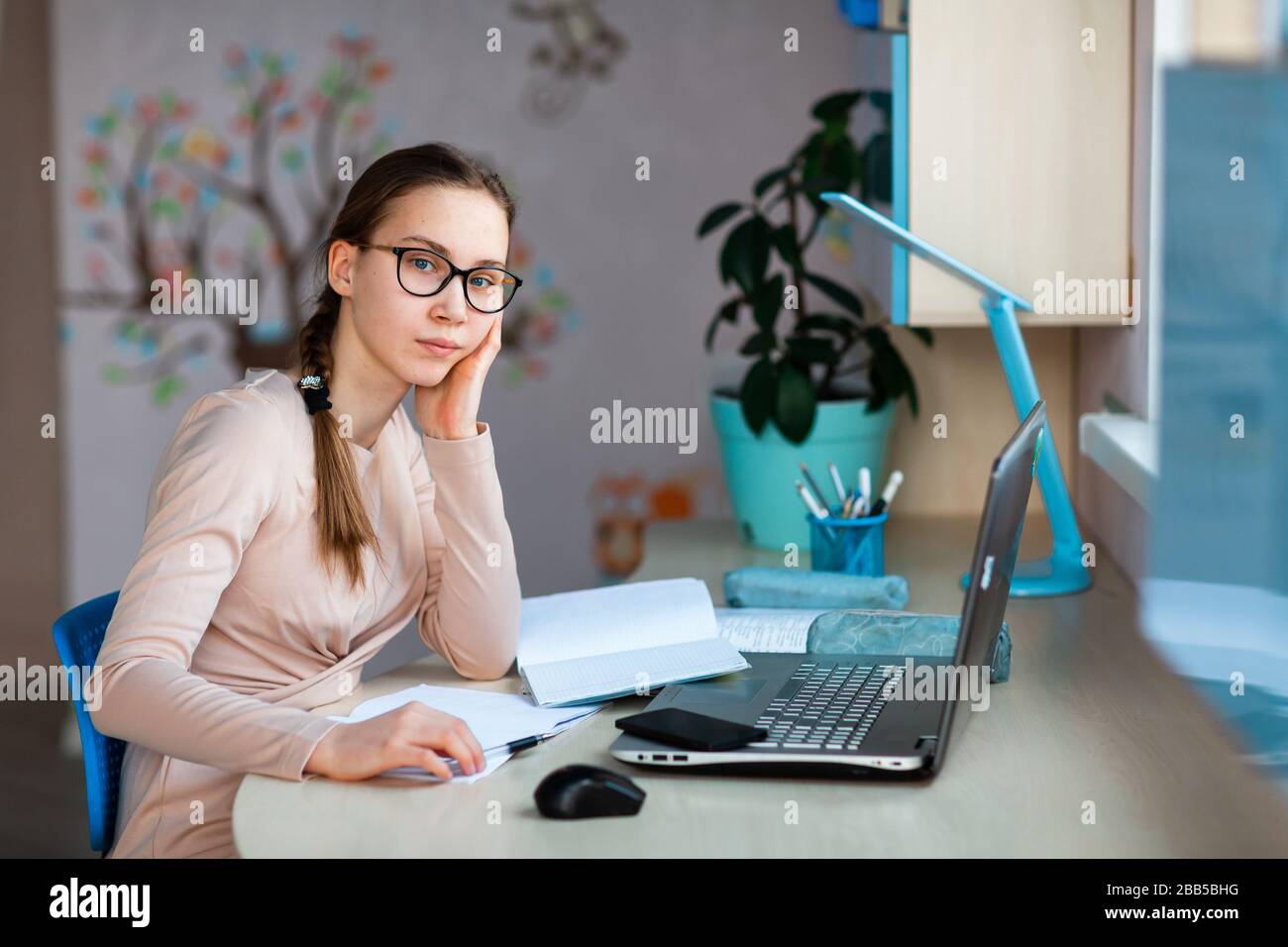 Beautiful young school girl working at home in her room with a laptop ...