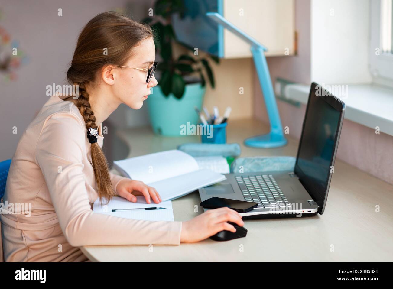 Beautiful young school girl working at home in her room with a laptop ...