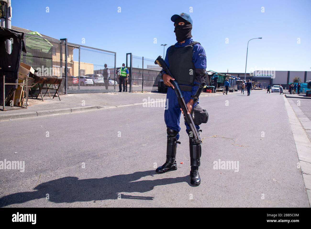 Cape Town, South Africa. 30th Mar, 2020. a member of TSU Protection Services stands guard inside a gate at a SASSA (South African Social Security Agency) paypoint in Philippi as hundreds of people wait their turn to enter to collect their money after the South African government declared a 21 day COVID-19 lockdown as part of the State of National Disaster declaration by President Cyril Ramaphosa. The Health Ministry has asked residents to observe the regulations, practise hygiene, stay at home and practise social distancing. Credit: Roger Sedres/Alamy Live News Stock Photo