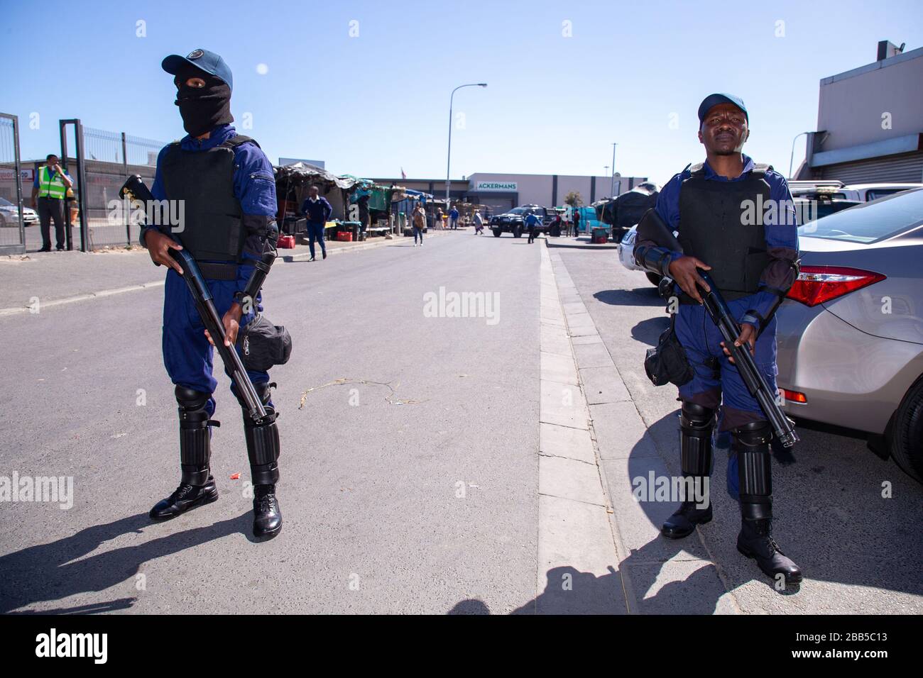 Cape Town, South Africa. 30th Mar, 2020. members of TSU Protection Services stand guard inside a gate at a SASSA (South African Social Security Agency) paypoint in Philippi as hundreds of people wait their turn to enter to collect their money after the South African government declared a 21 day COVID-19 lockdown as part of the State of National Disaster declaration by President Cyril Ramaphosa. The Health Ministry has asked residents to observe the regulations, practise hygiene, stay at home and practise social distancing. Credit: Roger Sedres/Alamy Live News Stock Photo