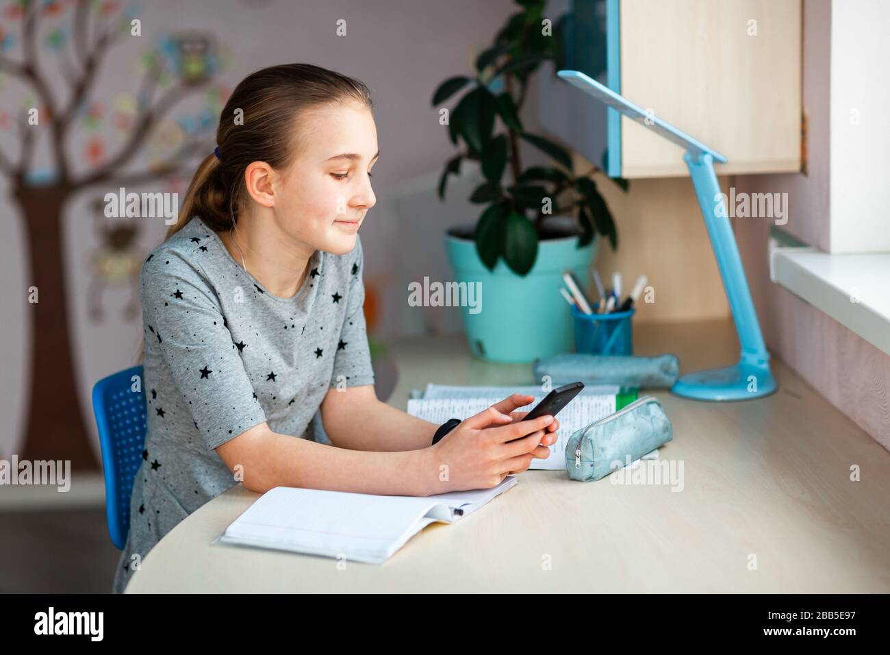 Beautiful young school girl working at home in her room with class ...
