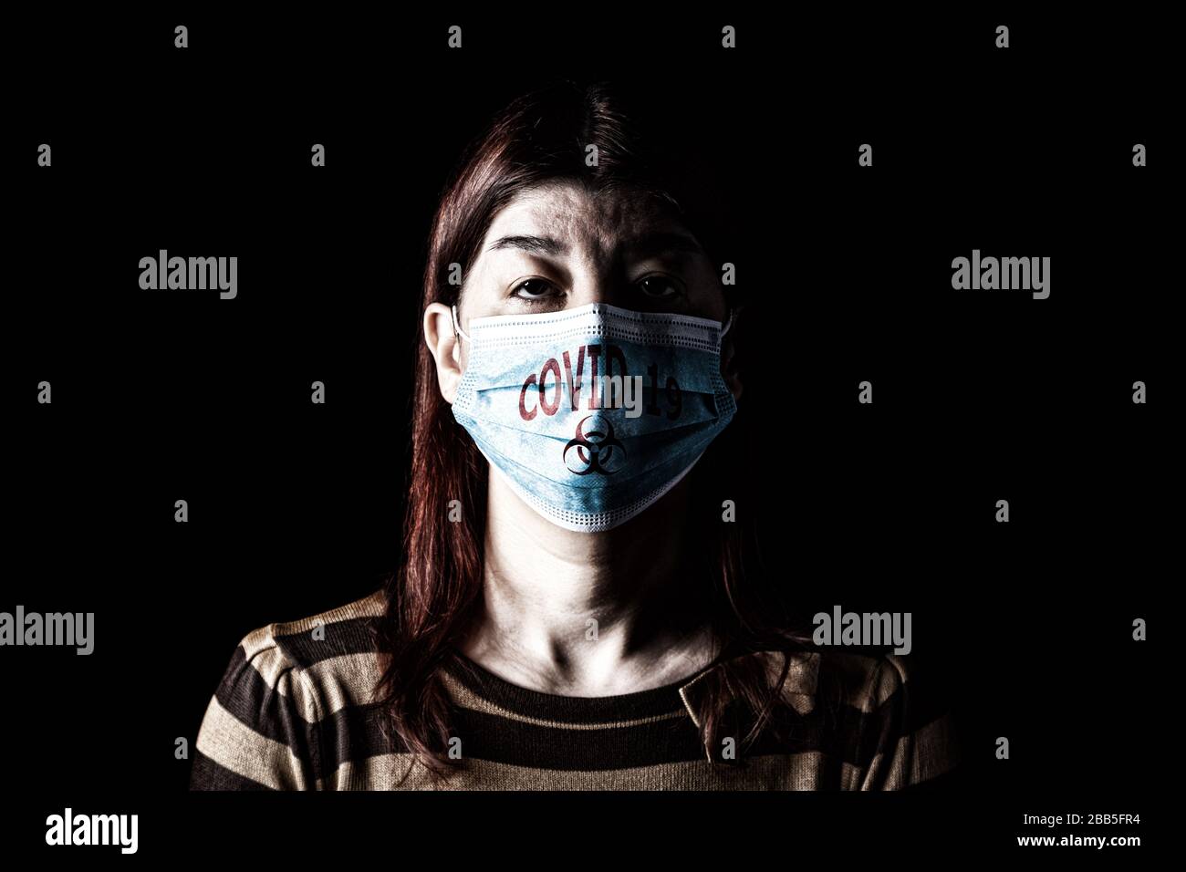 Woman with surgical mask. Biohazard and COVID-19, aka Coronavirus symbol. Pandemic or epidemic and scary, fear or danger concept. Black Background Stock Photo