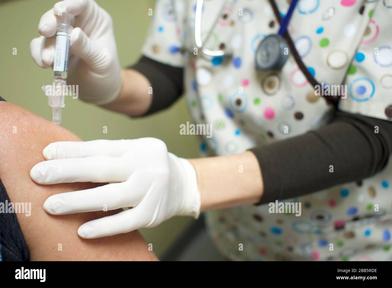 Nurse giving patient a vaccine in the bicep. Gloved hand, surgical scrubs injecting hypodermic needle into patient. Covid-19, Coronavirus protection. Stock Photo