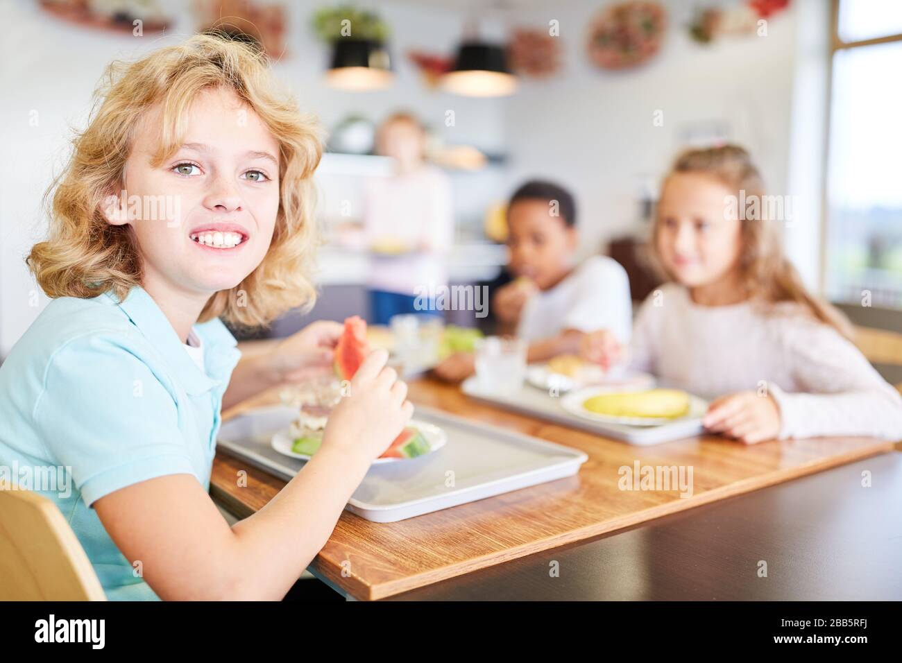 Happy children have lunch together in the canteen of a primary school Stock Photo