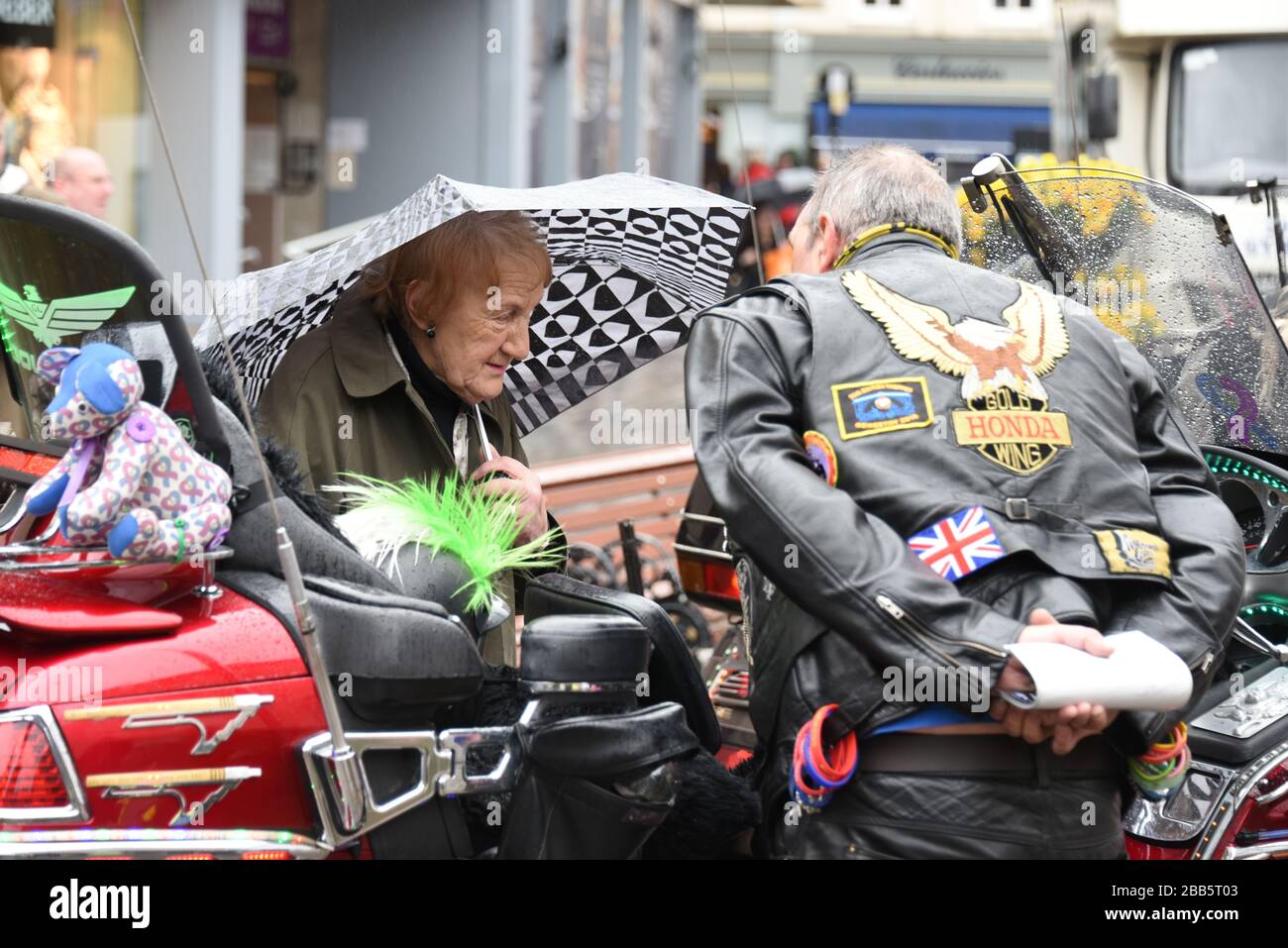 Elderly woman talking to a male biker while looking at a Honda Goldwing motorcycle parked in Shrewsbury's Town Square in the rain. Stock Photo