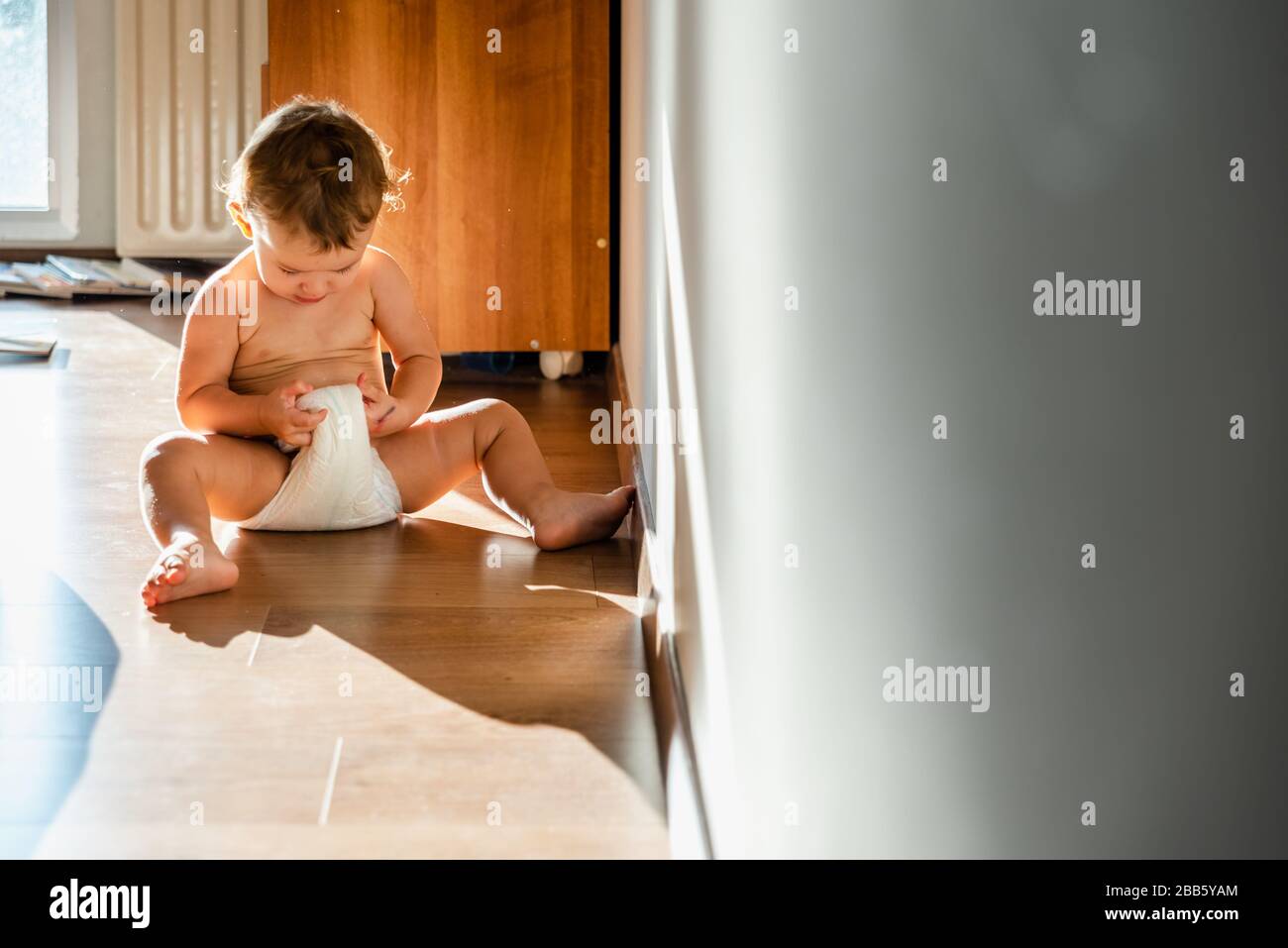 Baby girl in the morning wakes up and checks her wet diaper curiously. Stock Photo