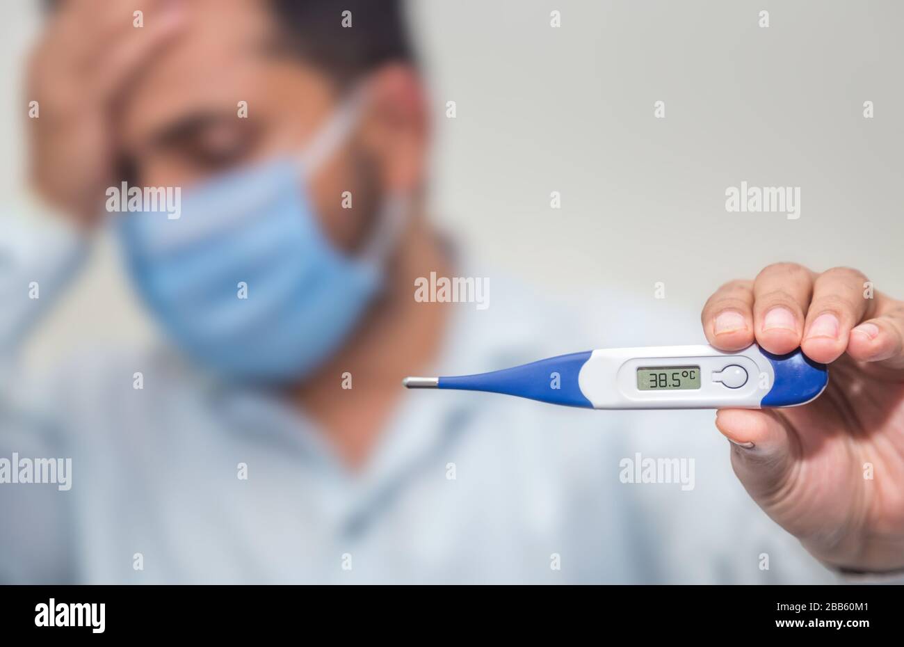 Novel corona virus COVID-19 -Sad man with tensed face holding digital thermometer, wearing a disposable mask, measuring body temperature. concept of c Stock Photo