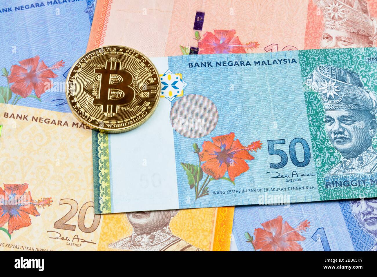 Close-up on a golden Bitcoin coin on top of a stack of Malaysian Ringgit banknotes. Stock Photo