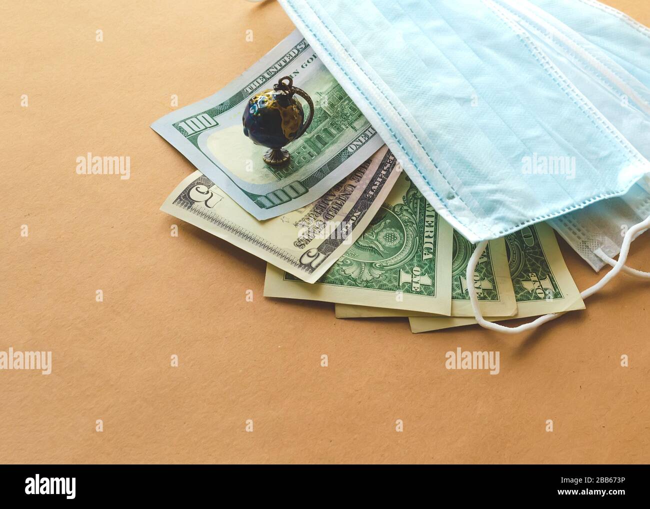 US paper currency with blue medical disposable protective masks and small globe on a brown background. Coronavirus concept Stock Photo