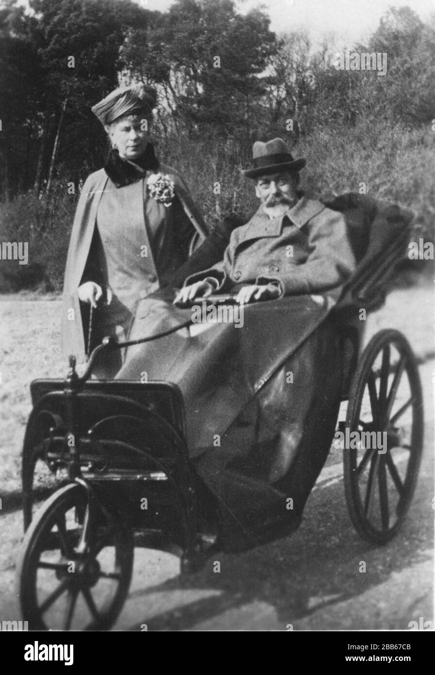 King George V  (1865-1936) with Queen Mary (Mary of Teck) (1867-1953), about 1929.  The King had developed chronic obstructive pulmonary disease by the mid-1920s. In this fine three-wheel wheelchair, he was resting a the seaside resort, Bognor. Text on this photo card says, "Kodak, Ltd will devote the whole of the profits derived from the sales of these postcards to King Edward's Hospital Fund for London."   To see my Royals-related vintage images, Search:  Prestor  vintage  Royal  vehicle Stock Photo