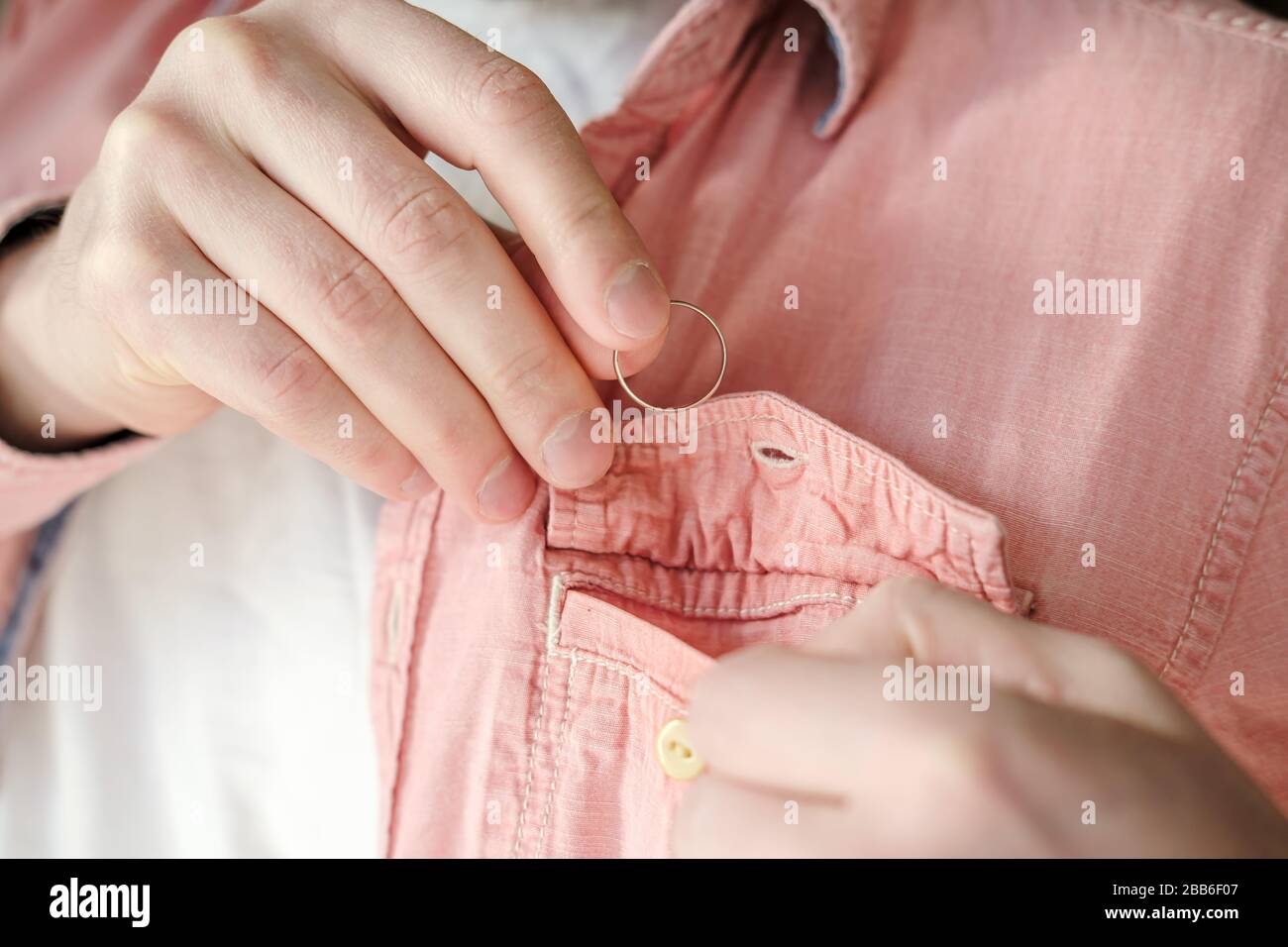 Hands of a man who took off a golden wedding ring and puts it in shirt pocket to hide his marital status from mistress. Stock Photo