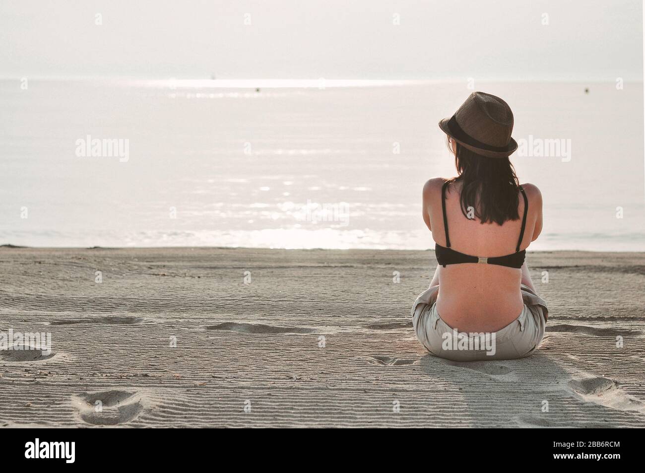 Rear view of a woman sitting on beach looking out to sea, Majorca, Balearics, Spain Stock Photo
