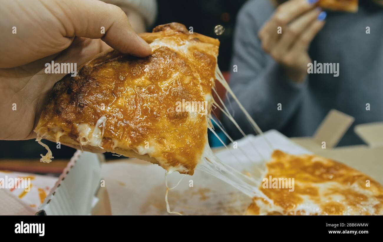 Mother and daughter eat pizza cheese four. Close up of young woman eating pizza and chewing in outdoor restaurant. Girl hands taking pieces pizza. Stock Photo