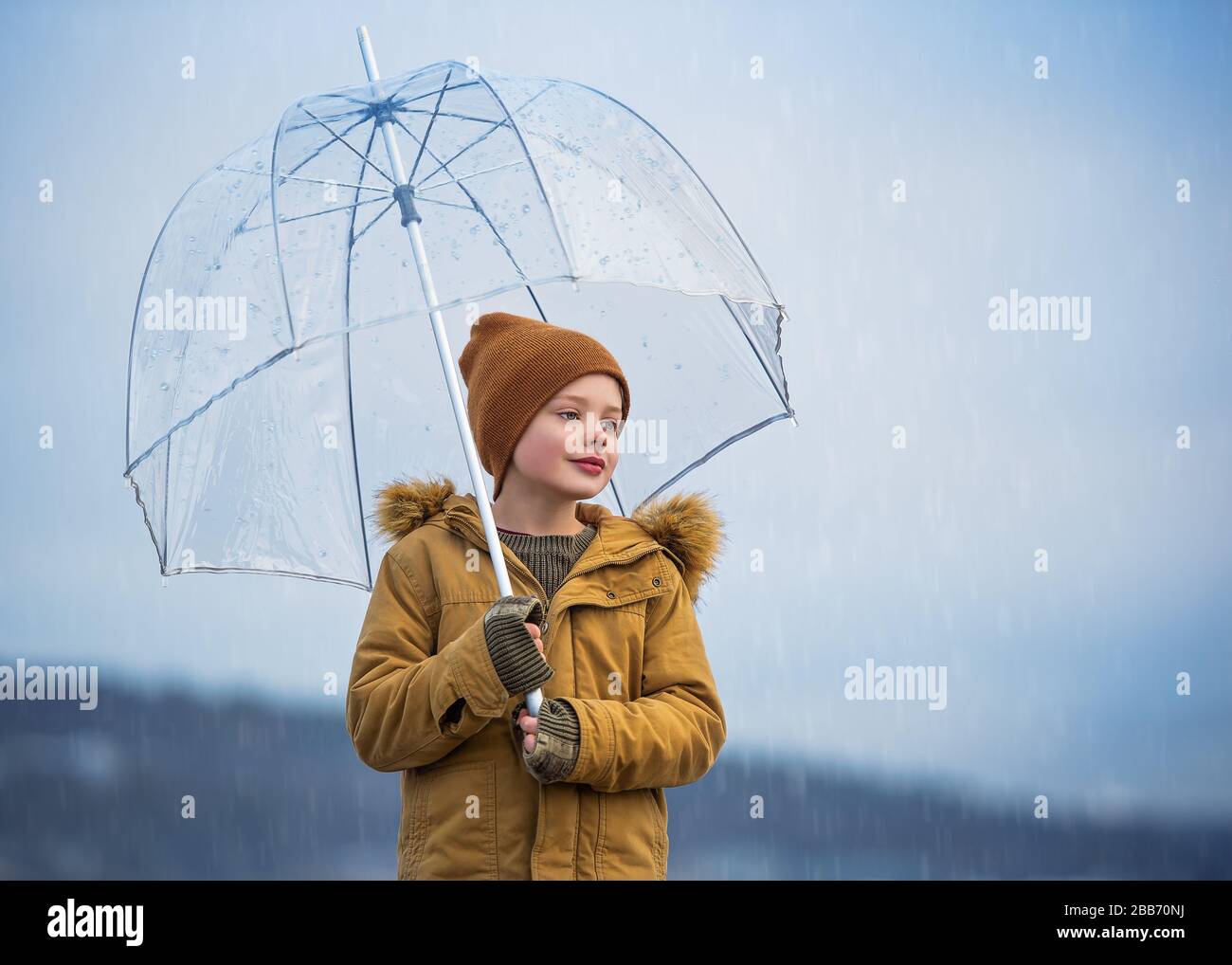 Smiling Boy standing under an umbrella in the rain, Bedford, Halifax, Nova Scotia, Canada Stock Photo