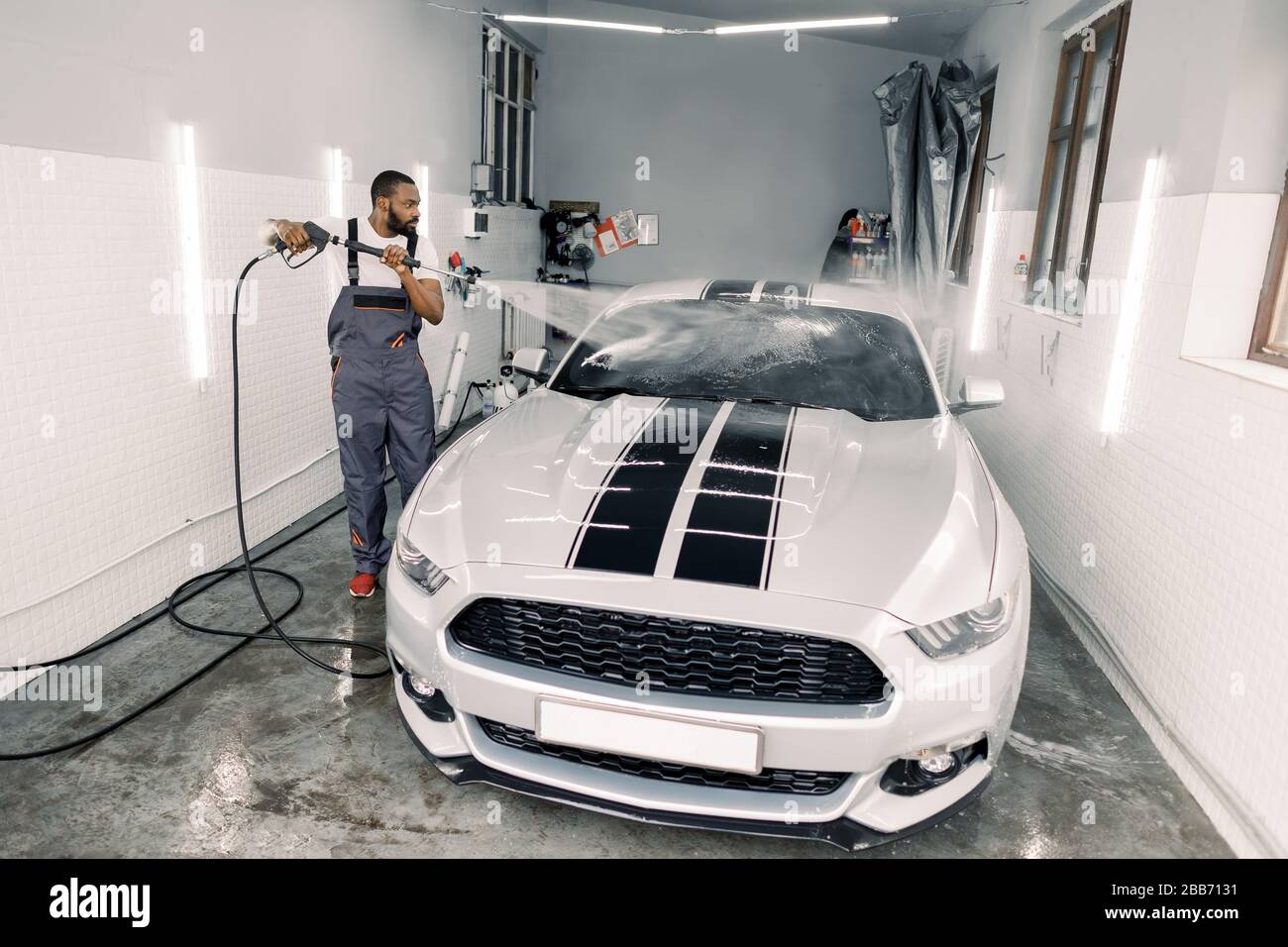 Cleaning car using high pressure water. Handsome young African man worker, wearing protective