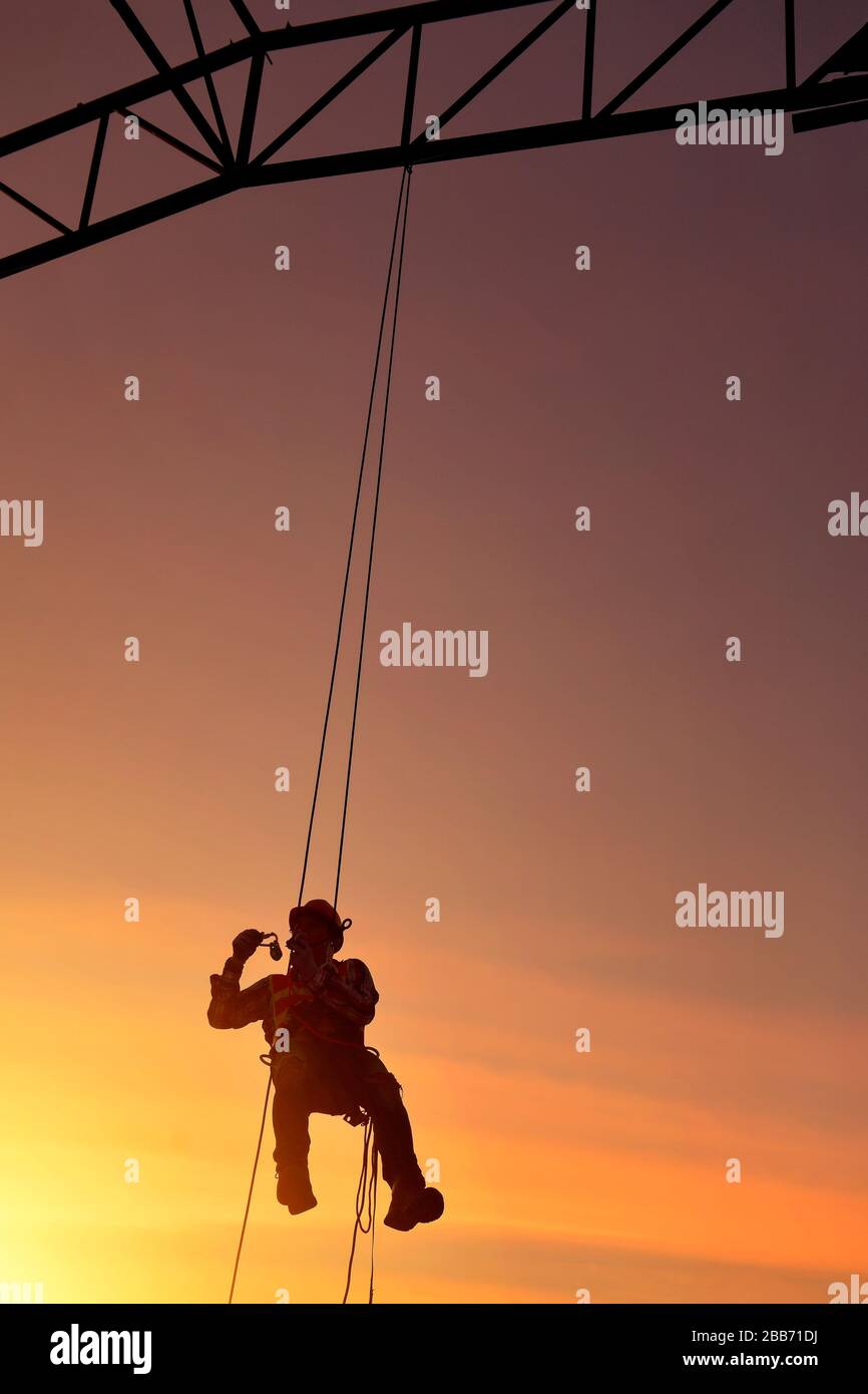 Silhouette of a construction worker hanging on safety harness on a construction site, Thailand Stock Photo