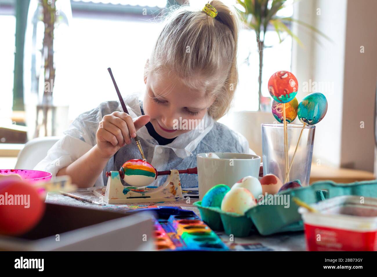 Portrait of adorable blonde girl at home painting easter eggs Stock Photo