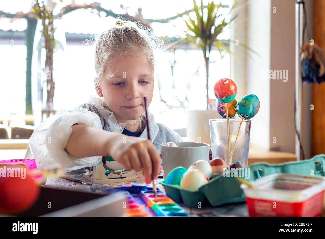 Portrait of adorable blonde girl at home painting easter eggs Stock Photo