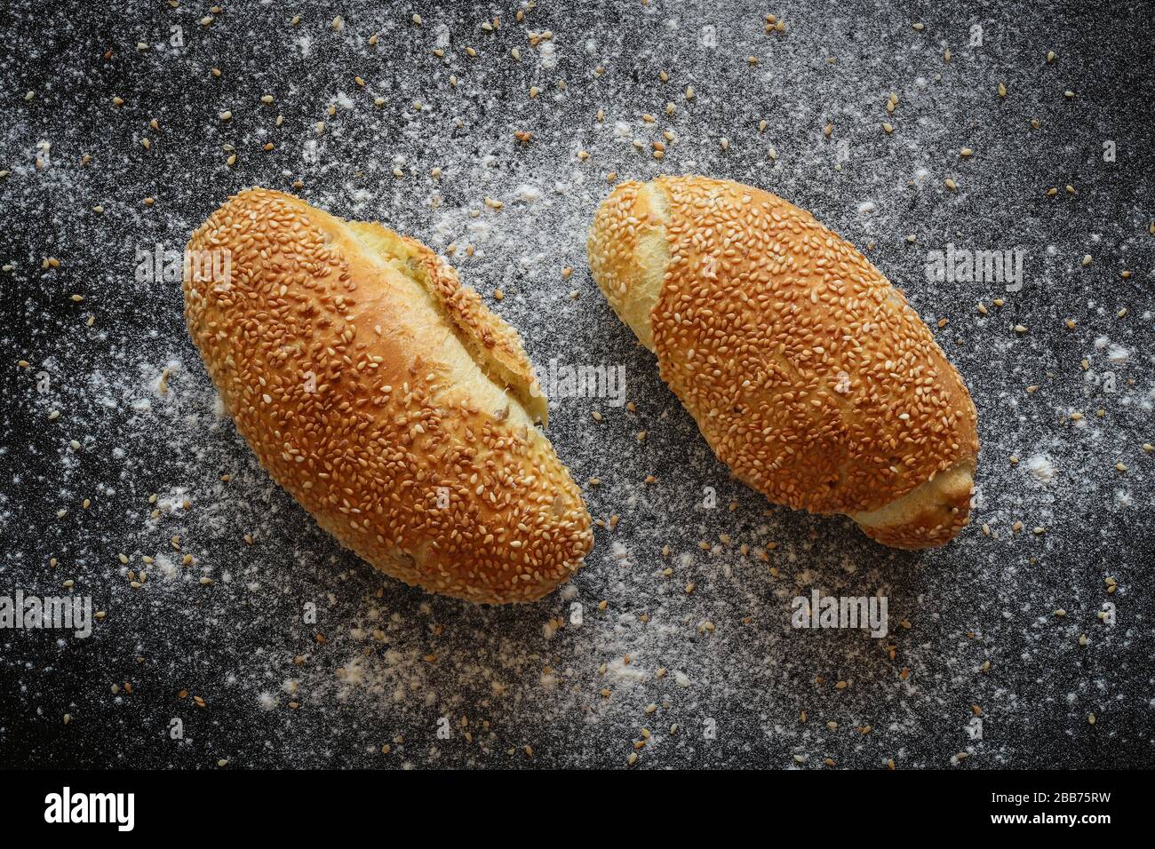 Flat lay shot of fwo fresh corn bread rolls with sesame seeds on black sprinkled with flour and sesame seeds backgroud Stock Photo