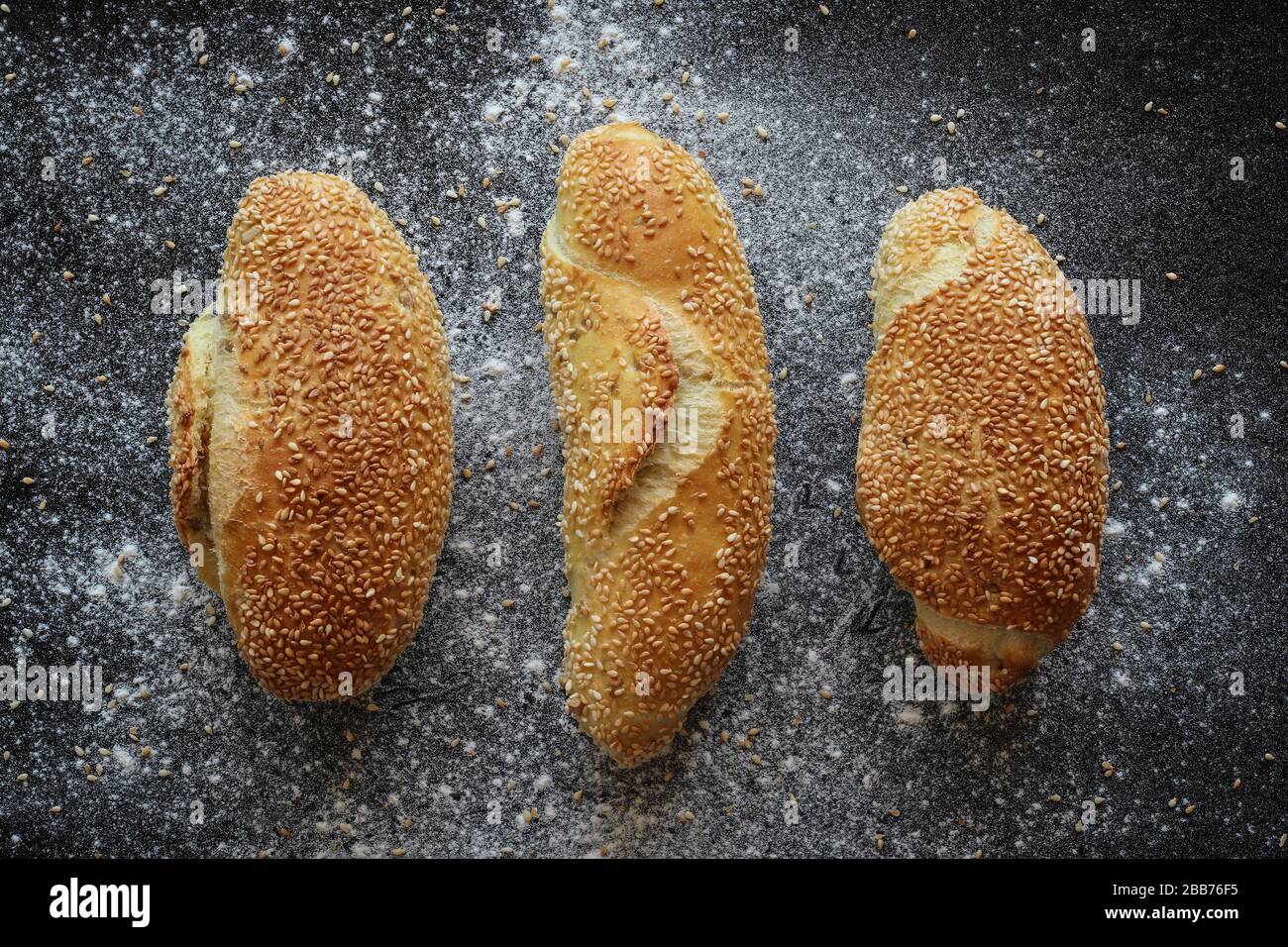 Flat lay shot of three fresh corn bread rolls with sesame seeds on black sprinkled with flour and sesame seeds backgroud Stock Photo
