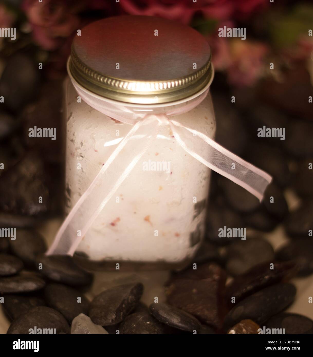 Sugar scrub jar with ribbon surrounded by black rock Stock Photo