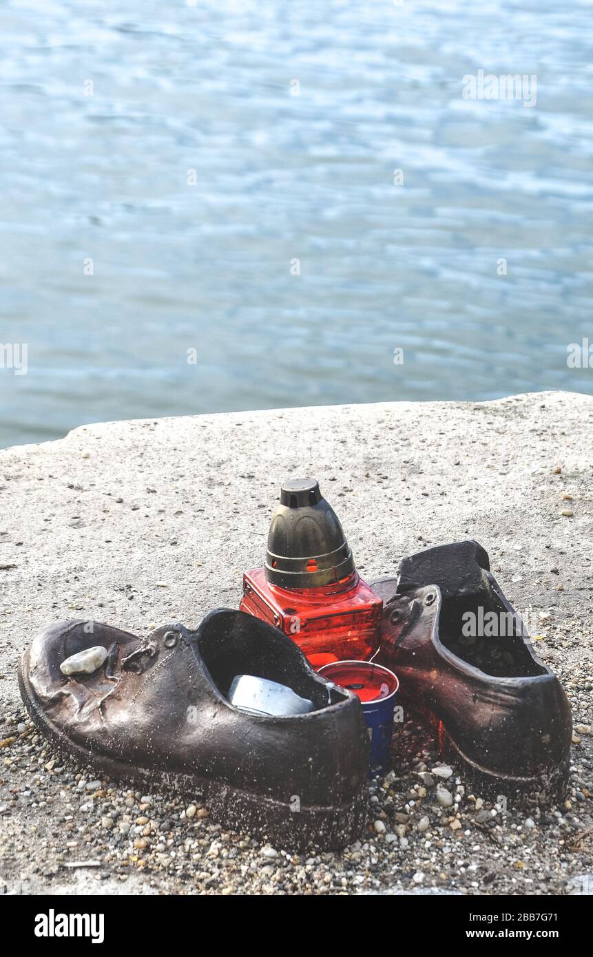 Budapest, Hungary - Nov 6, 2019: Shoes on the Danube Bank. Monument to honour the Jews who were killed by fascists during World War II. Iron shoes, red candle. Blurred Danube in the background. Stock Photo