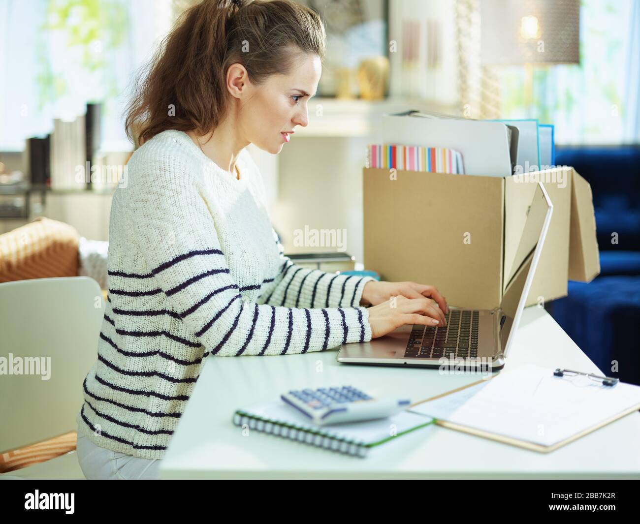 modern middle age business woman in striped sweater in temporary home office in the modern house in sunny day working. Stock Photo