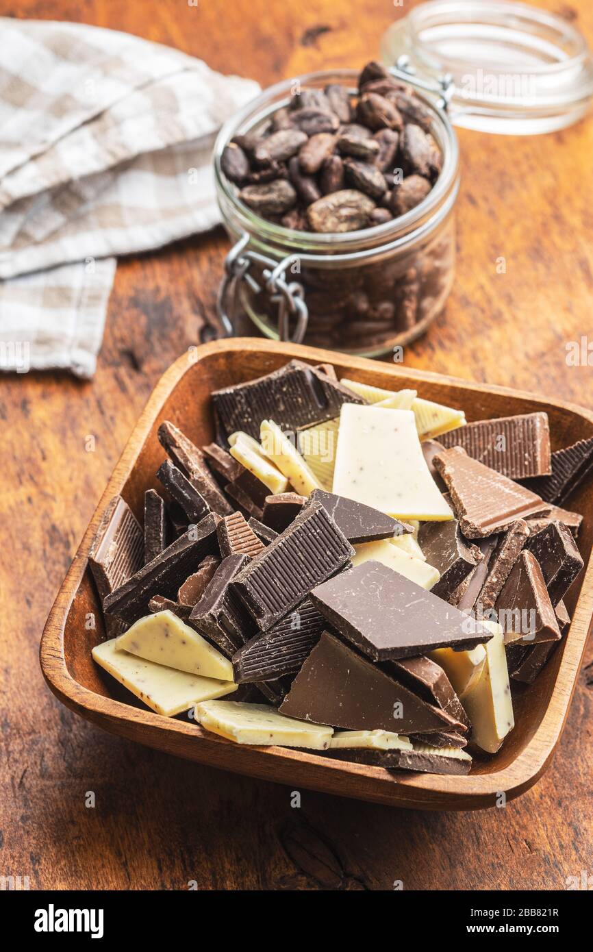 Broken white, milk and dark chocolate bars in bowl on wooden table. Stock Photo