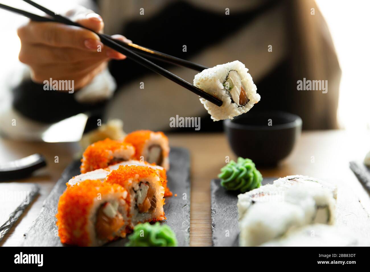 Beautiful young woman eating sushi roll at cafe. Woman eating sushi set with chopsticks on restaurant. Stock Photo