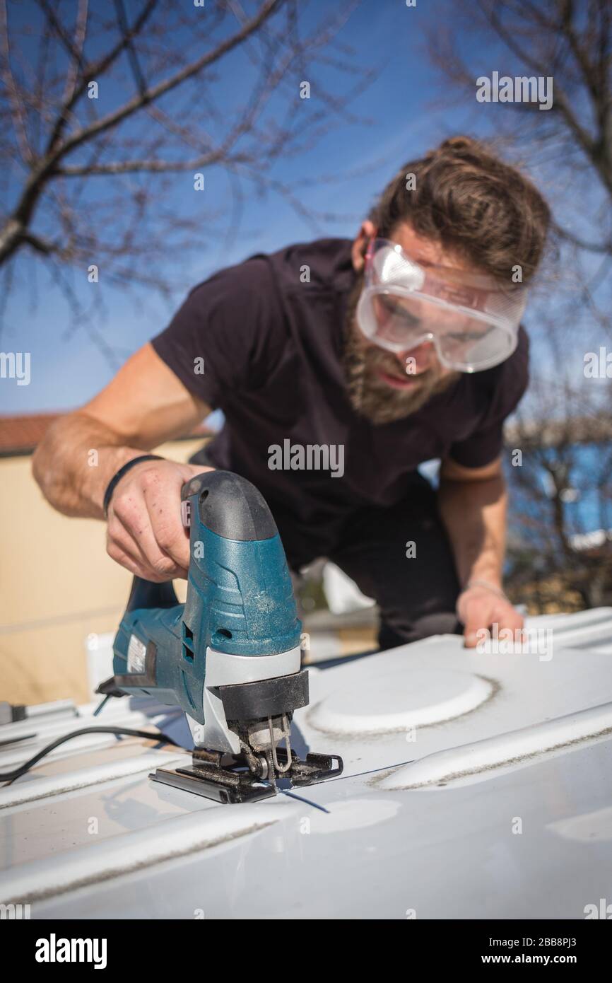 Man cutting a hole into the roof of his camper van Stock Photo
