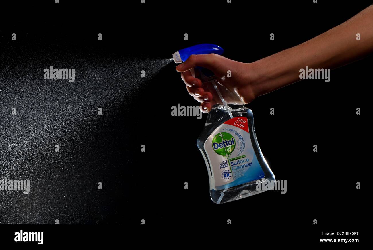 Dettol anti bacterial surface cleaner bottle hand held on a black background showing fine spray of liquid Stock Photo