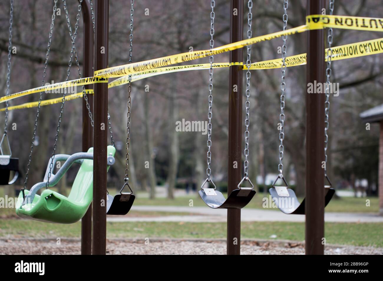 Empty swing set with caution tape to close off playground to children to help fight the coivd-19 disease. Close up empty swing set playground. Stock Photo