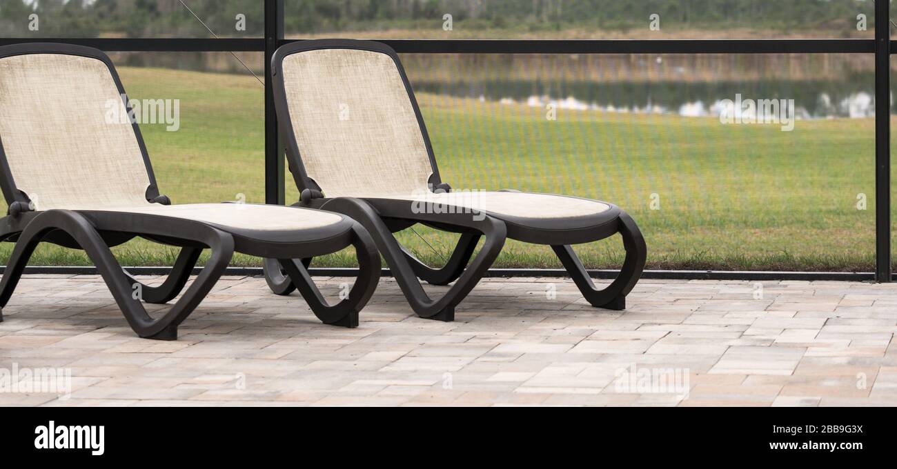 Two tan lawn chairs inside a screened pool area. Stock Photo