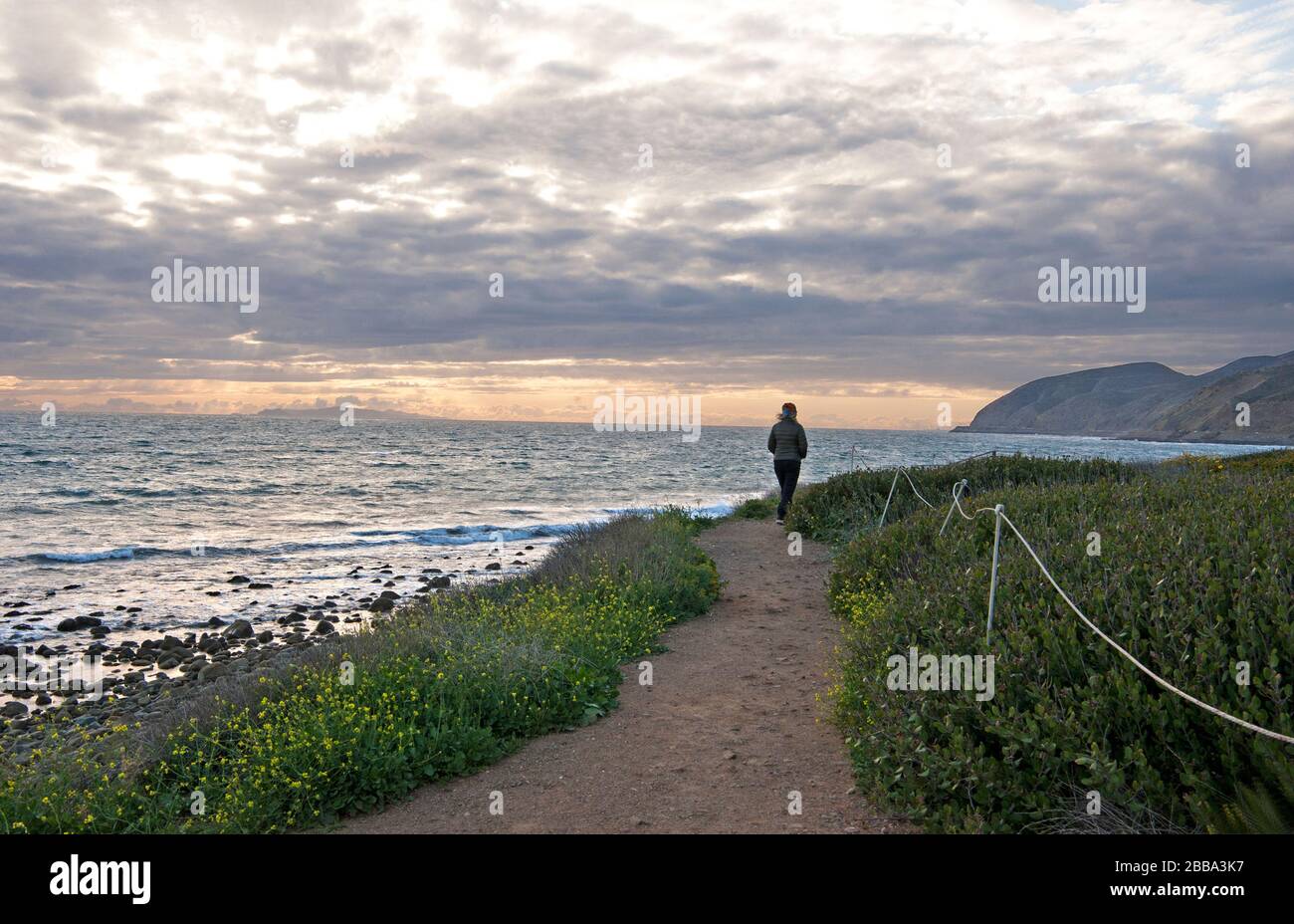 Woman walking on trail on cliffs above the Pacific Ocean at Malibu on the Southern California coast. Stock Photo