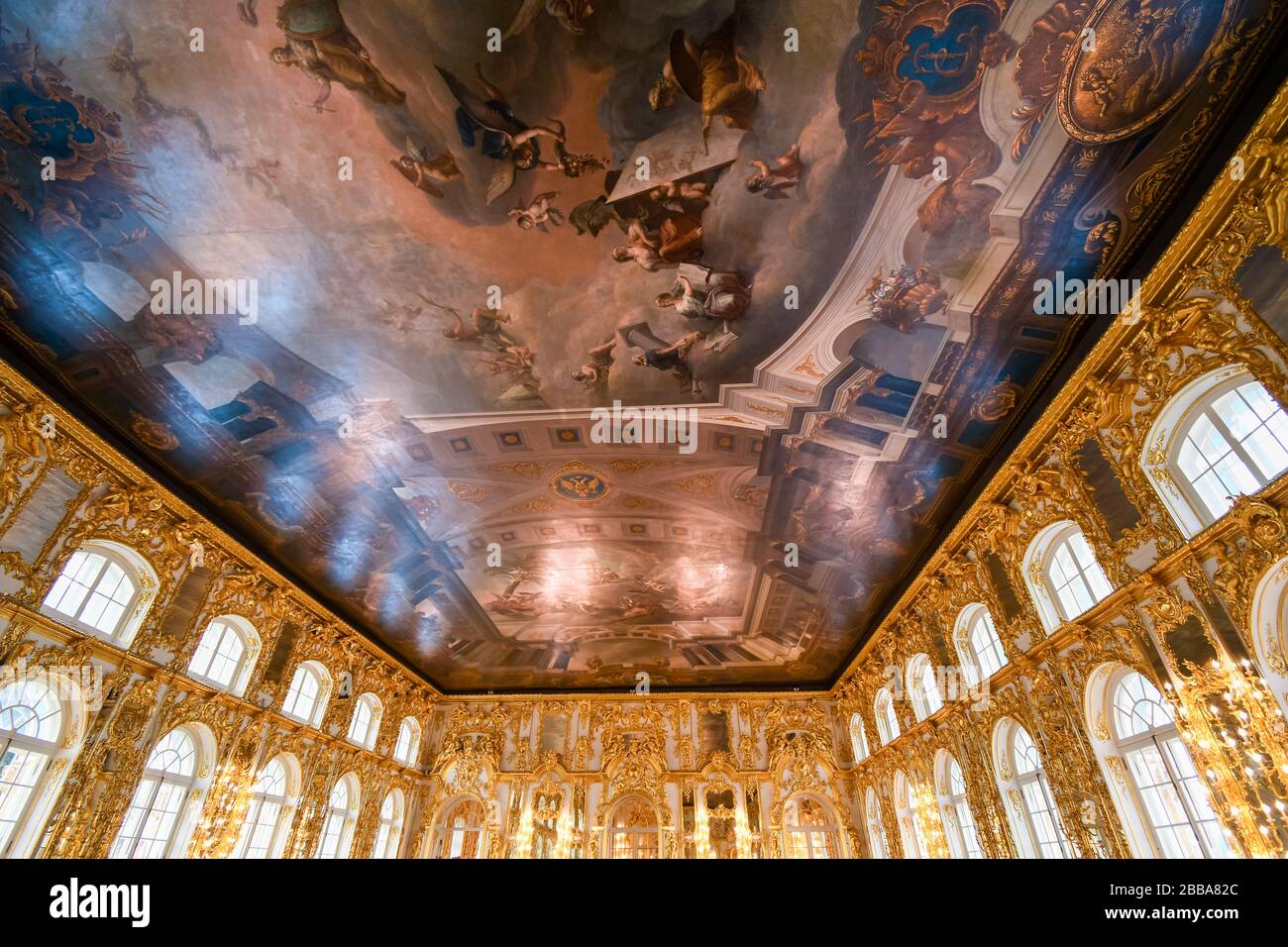 An ornate golden interior ballroom with a colorful painted ceiling inside the Rococo Catherine Palace at Pushkin near St. Petersburg, Russia. Stock Photo