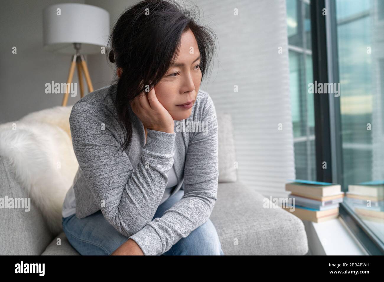 Sad Asian mature woman lonely at home self isolation quarantine for COVID-19 Coronavirus social distancing prevention. Mental health, anxiety depressed thinking senior chinese lady. Stock Photo