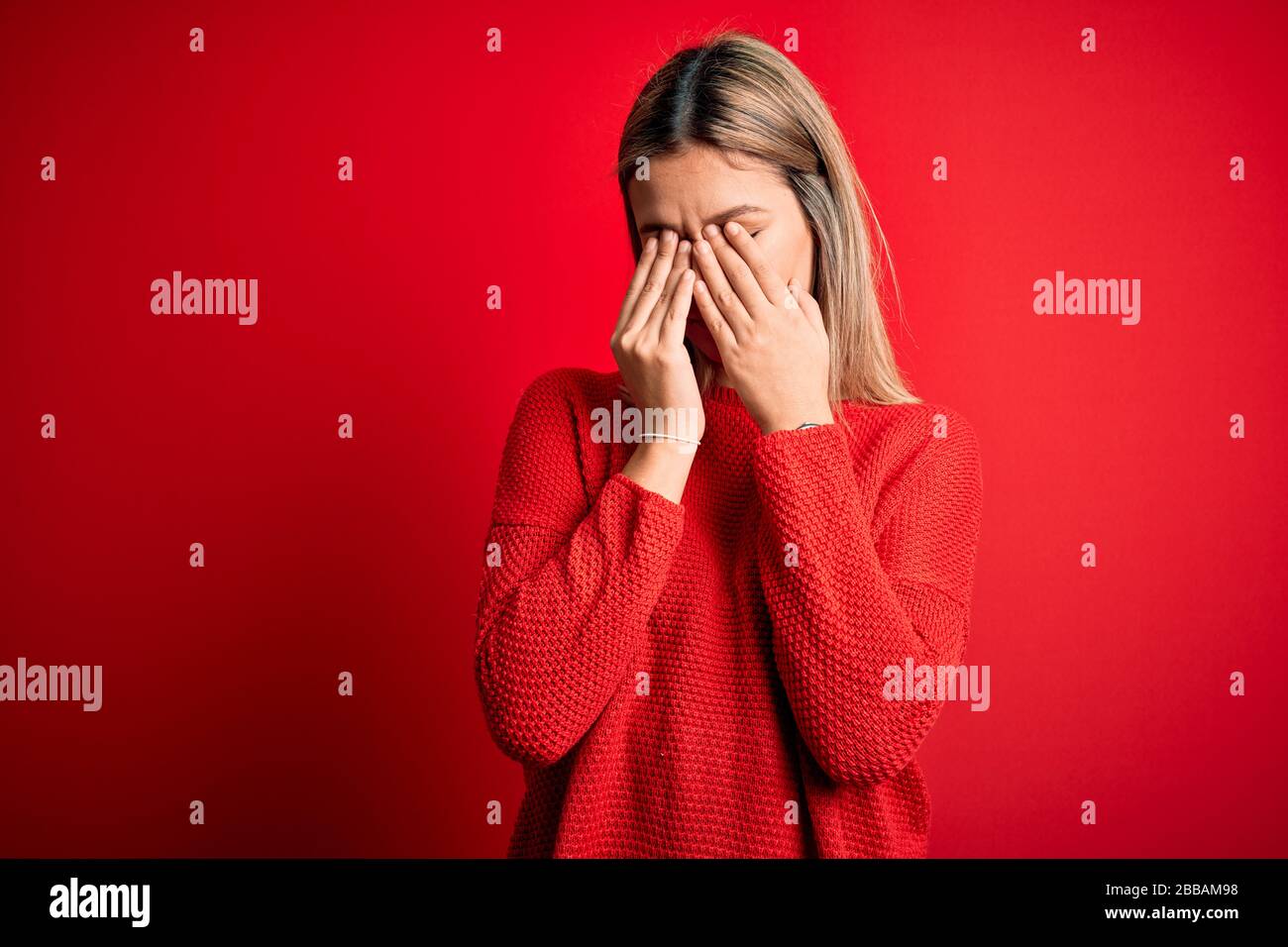 Young beautiful blonde woman wearing casual sweater over red isolated background rubbing eyes for fatigue and headache, sleepy and tired expression. V Stock Photo