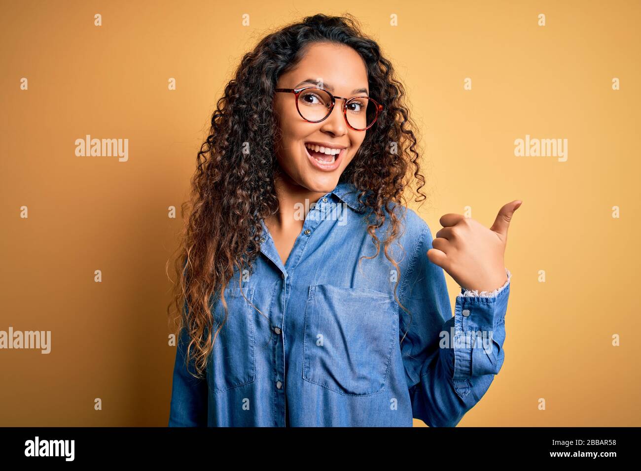 Beautiful woman with curly hair wearing casual denim shirt and glasses ...