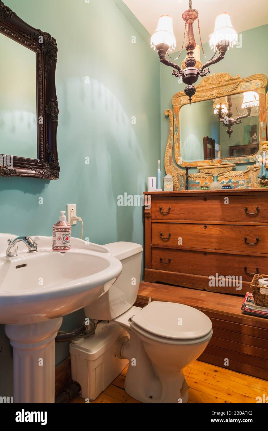 White pedestal sink with electric flush toilet, antique wooden mirror and dresser in bathroom with pinewood plank floorboards on upstairs floor inside an old circa 1830 Quebecois style country home, Quebec, Canada. This image is property released. CUPR0357 Stock Photo