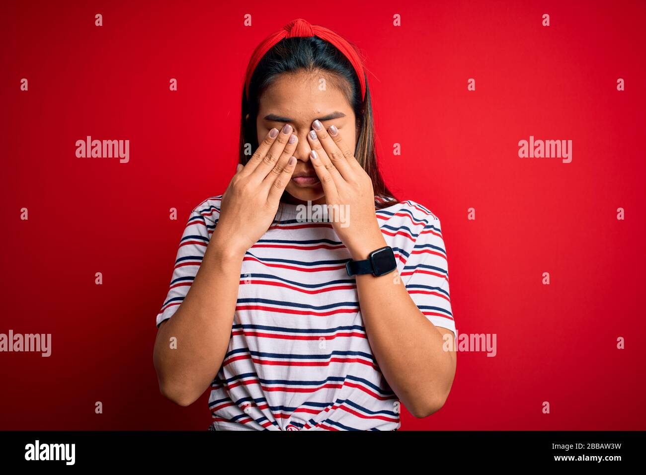 Young beautiful asian girl wearing casual striped t-shirt over isolated red background rubbing eyes for fatigue and headache, sleepy and tired express Stock Photo