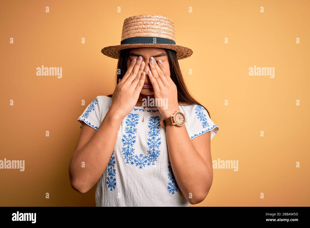 Young beautiful asian girl wearing casual t-shirt and hat standing over yellow background rubbing eyes for fatigue and headache, sleepy and tired expr Stock Photo