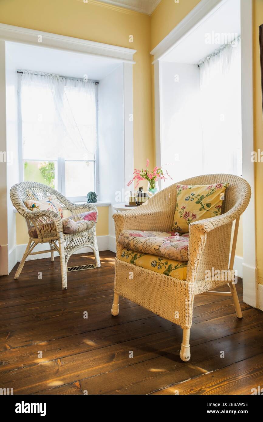 White wicker armchairs with flowery cushions and small round table in corner of living room with brown stained barn wood floorboards inside an old circa 1830 Quebecois style country home, Quebec, Canada. This image is property released. CUPR0357 Stock Photo