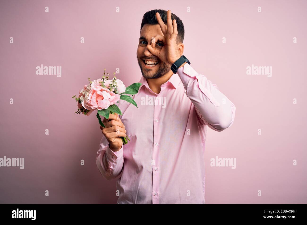 Young romatic man holding bouquet of spring flowers over pink isolatd ...