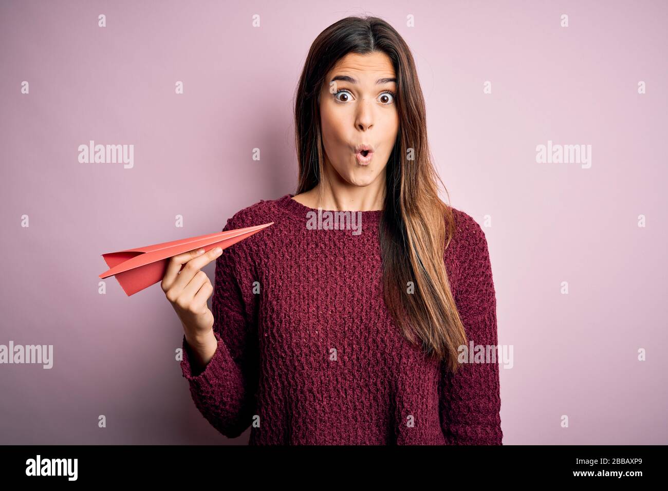 Afraid Paper Young beautiful girl holding paper plane standing over isolated pink ...