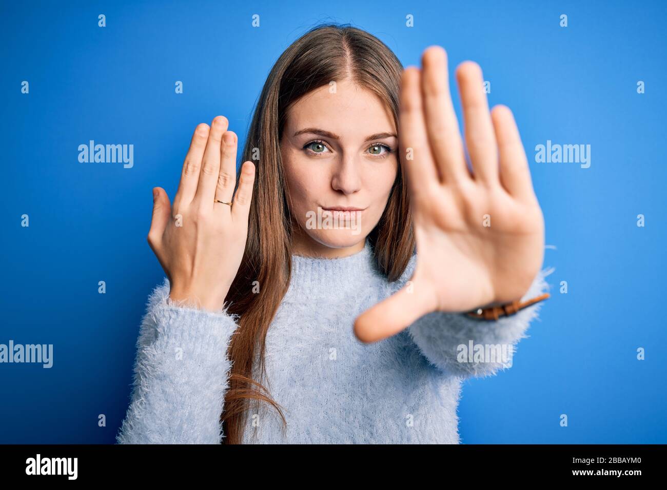 Young beautiful redhead woman wearing wedding ring on finger over blue