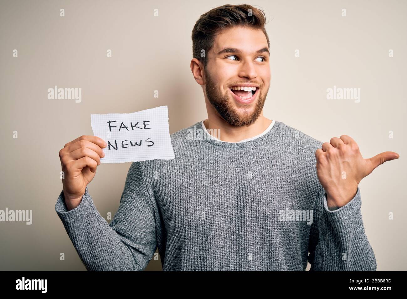 Young blond man with beard and blue eyes holding paper with fake news ...