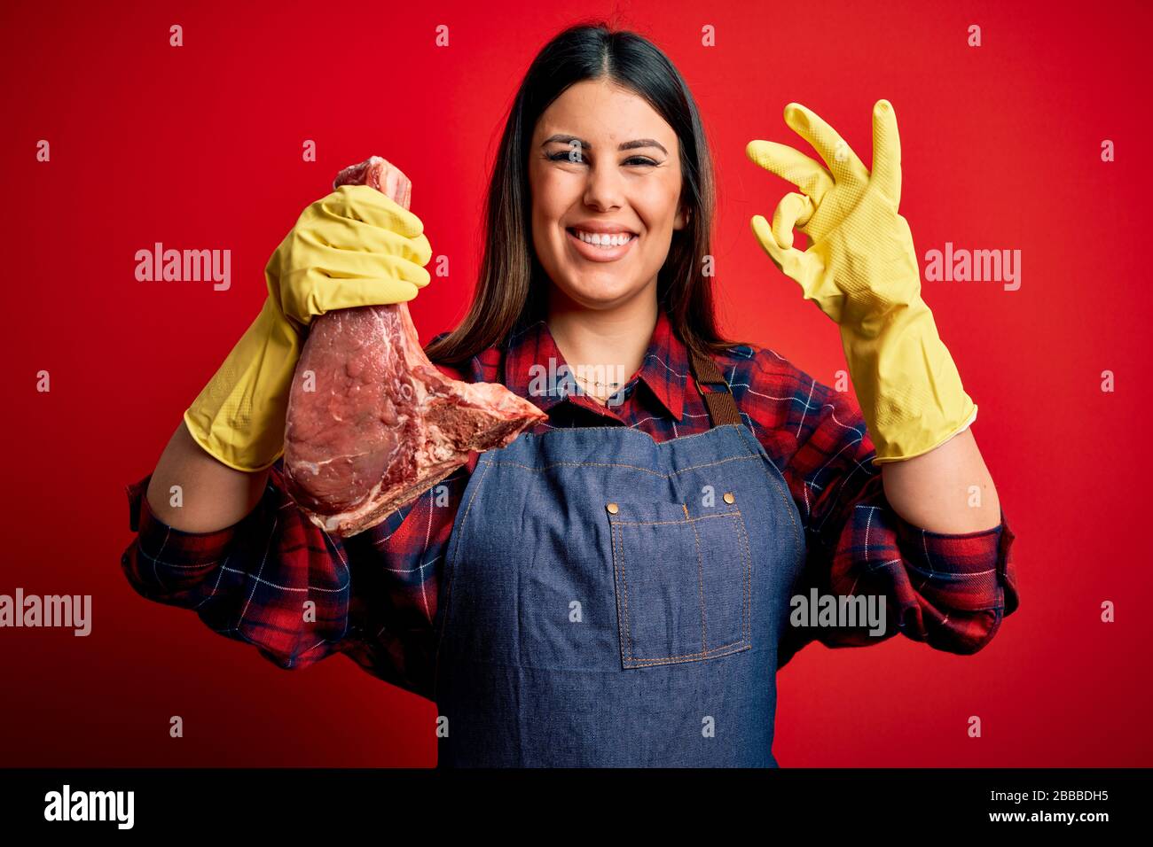 Young butcher woman holding fresh raw beef meat stake over red ...